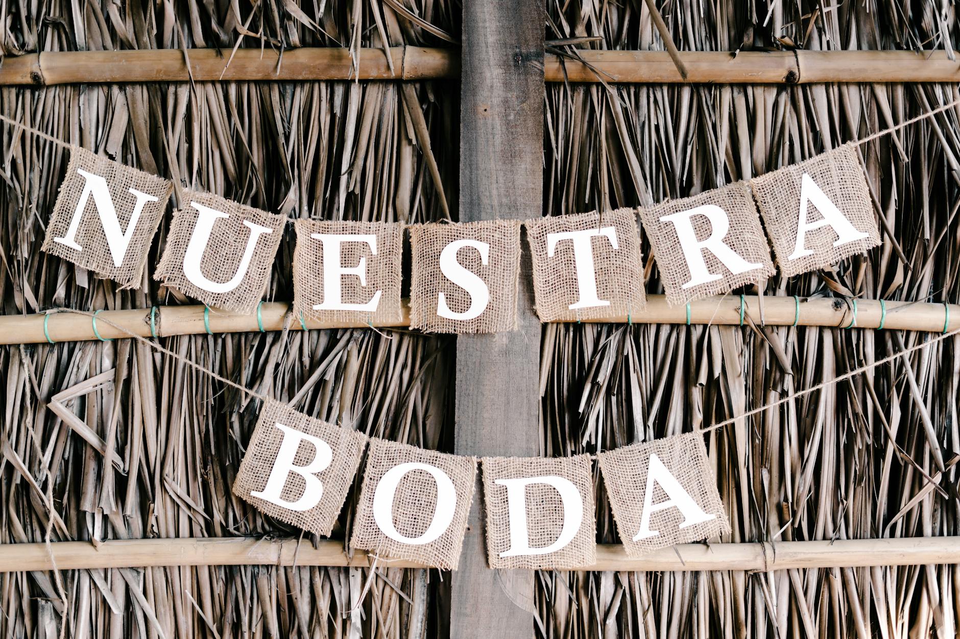 A close-up of a rustic wedding banner with burlap letters on a straw backdrop.