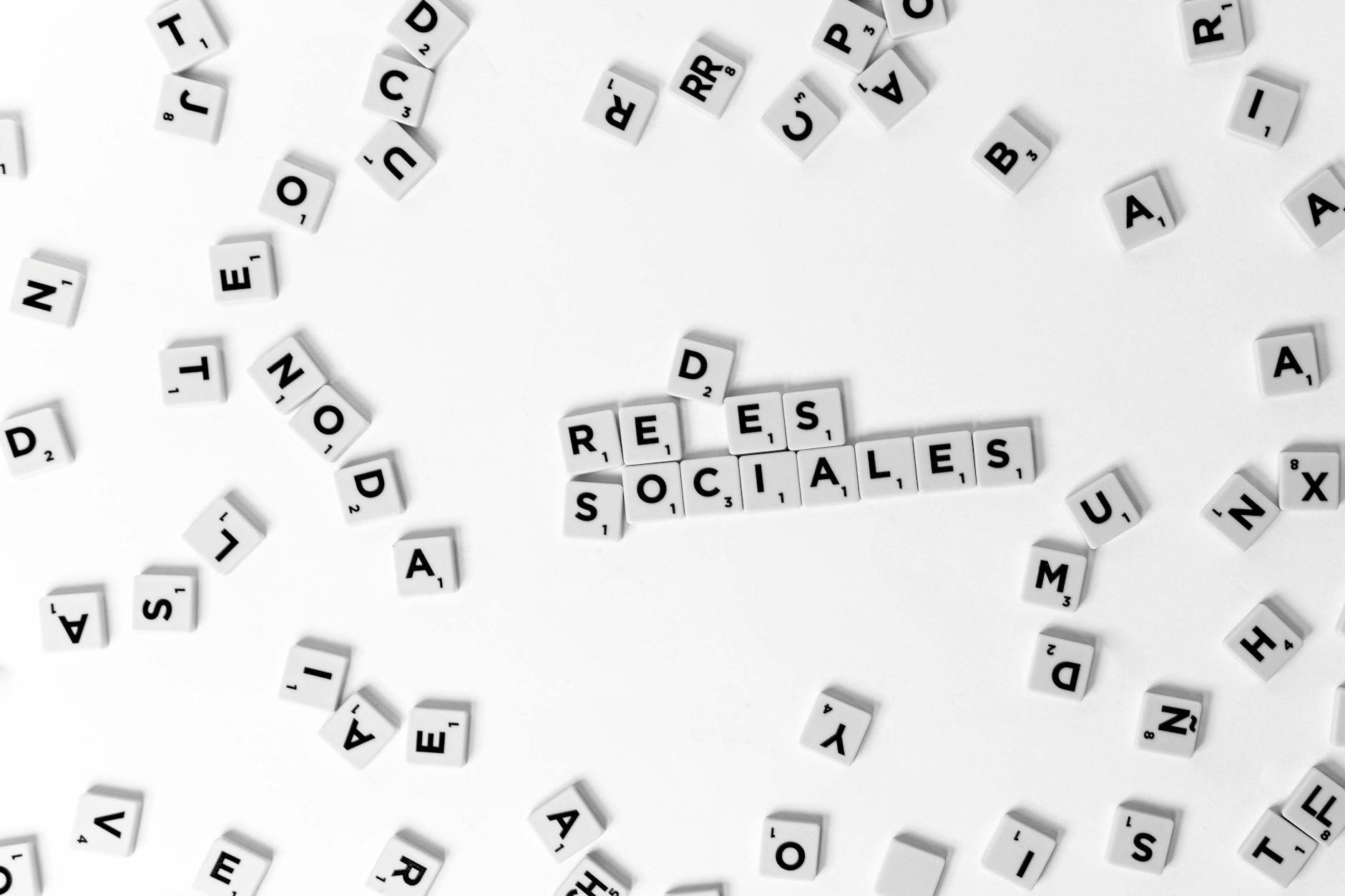 Scattered Scrabble tiles form 'Redes Sociales' on a white surface, emphasizing social media concepts.