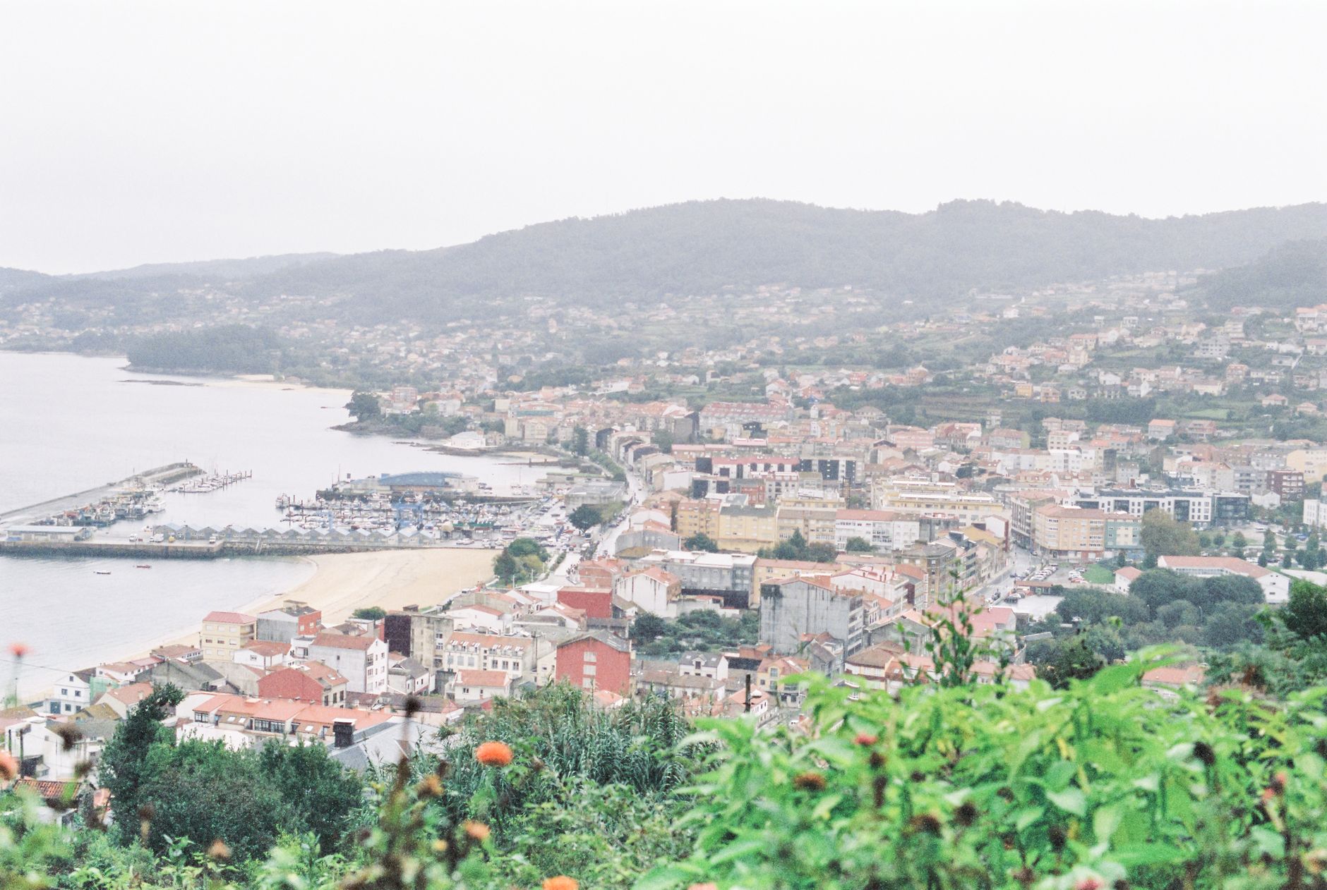 Aerial view of a picturesque coastal city with a harbor, surrounded by natural landscapes.