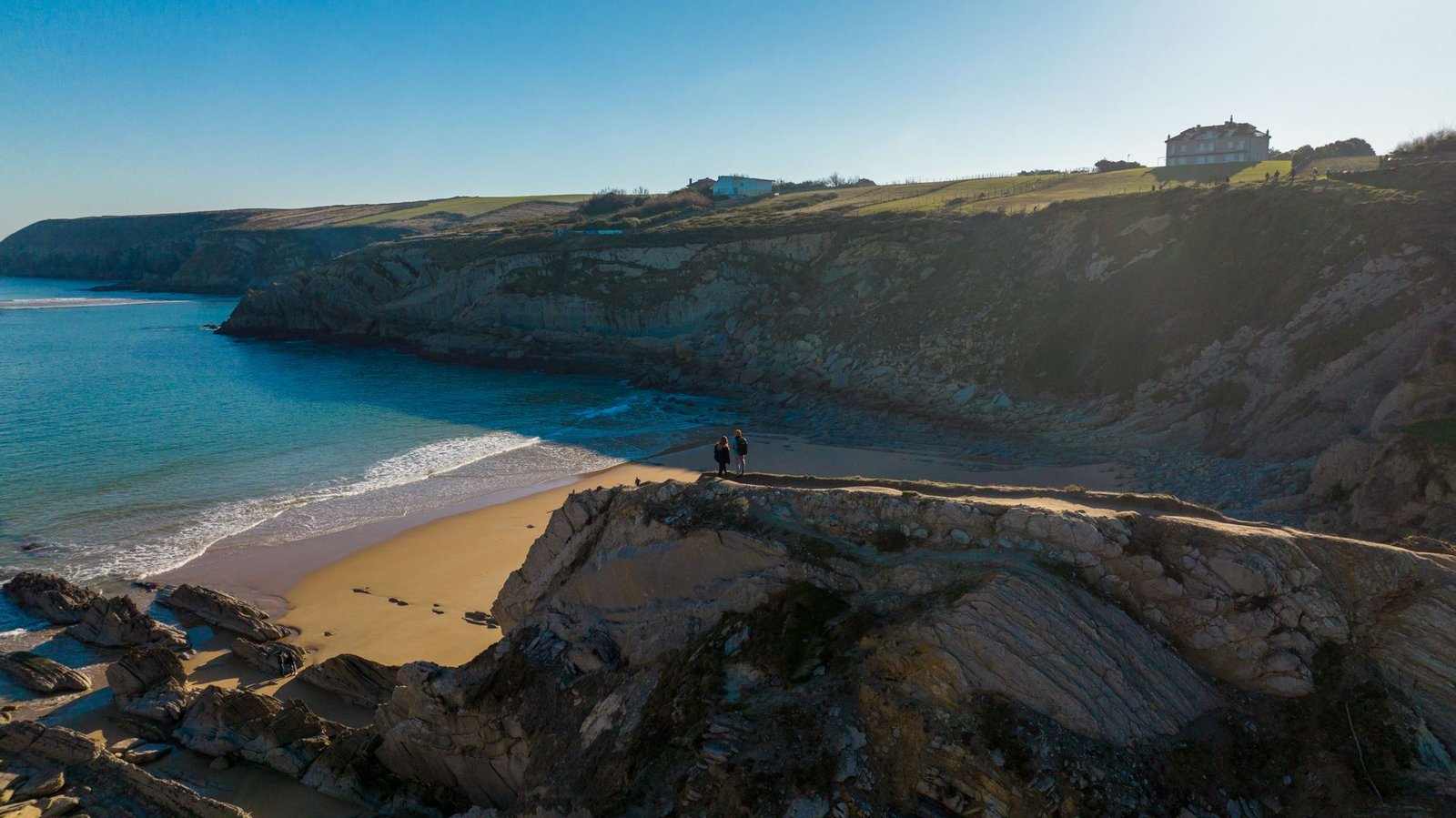 Aerial view of Cantabria's rugged coastline with cliffs and sandy beach. Captured during the day in vibrant colors.