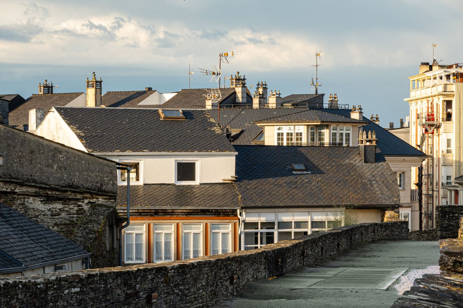 View of traditional European rooftops with chimneys and antennas in warm evening light.