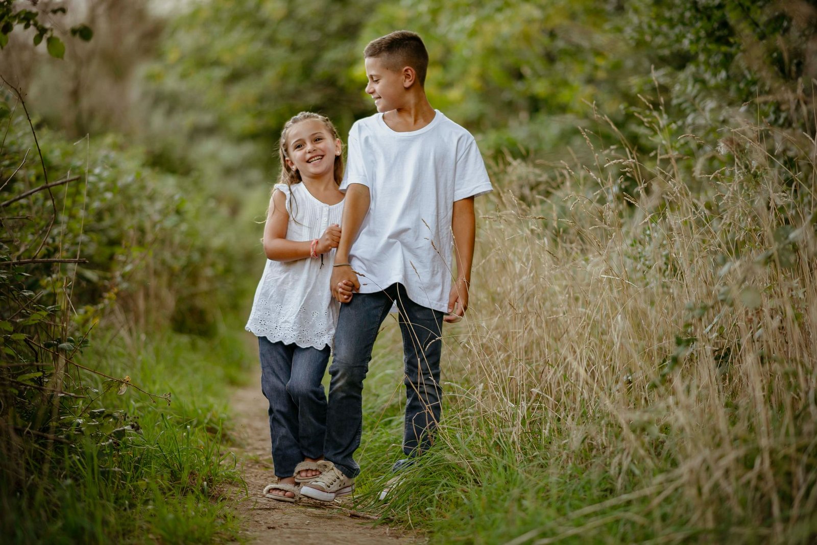 Brother and sister enjoying a peaceful walk on a lush nature path outdoors.