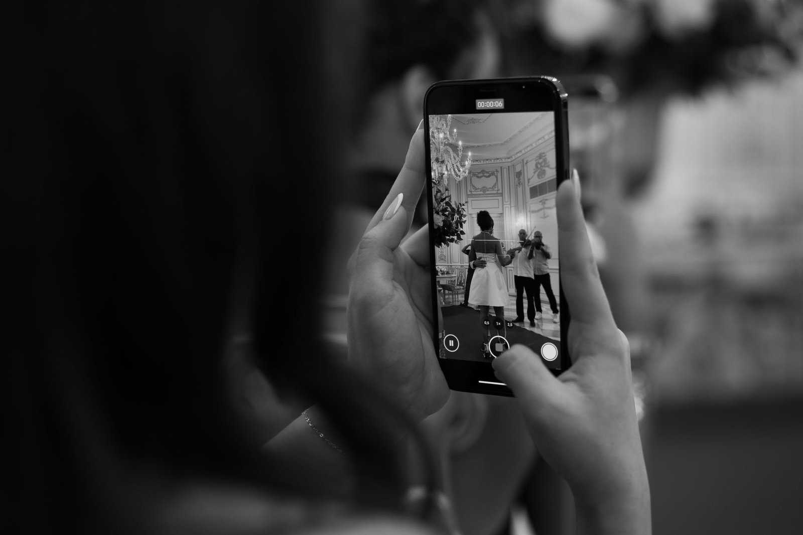 Black and white image of a smartphone capturing a formal event scene, featuring a woman and photographer.