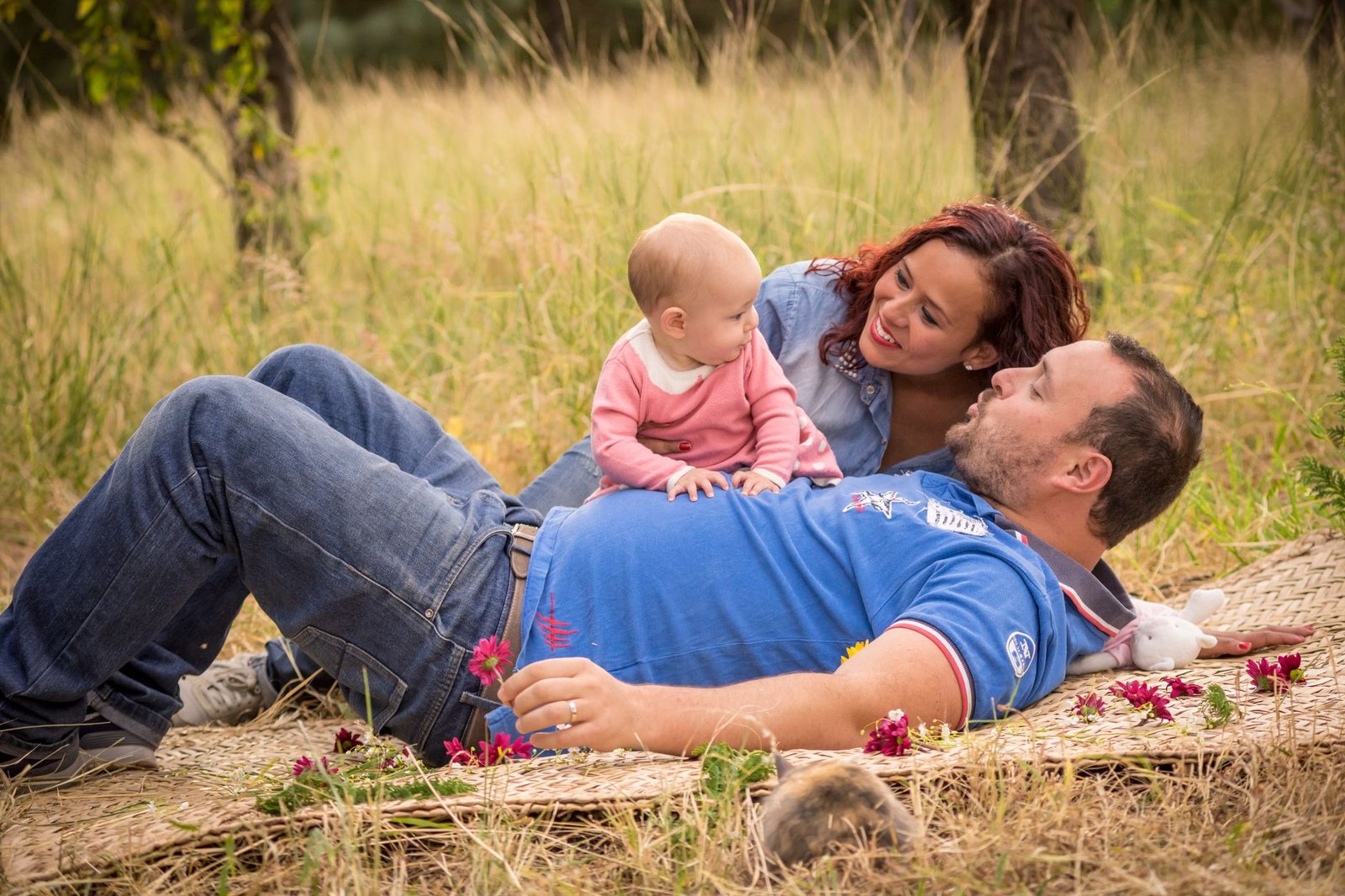 A family enjoys a relaxing picnic in a grassy field, focusing on bonding time with their baby.