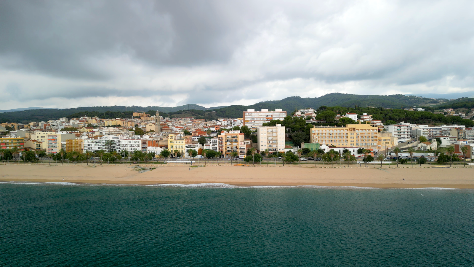 Aerial view of Canet de Mar beach with overcast sky and cityscape in the background.
